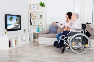 Elderly woman in wheelchair watching television with younger woman